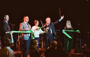 Thumbnail photo of Co Owners Steve Peters and Connor Delaney cut the ribbon on stage with Des Moines Mayor Connie Boesln