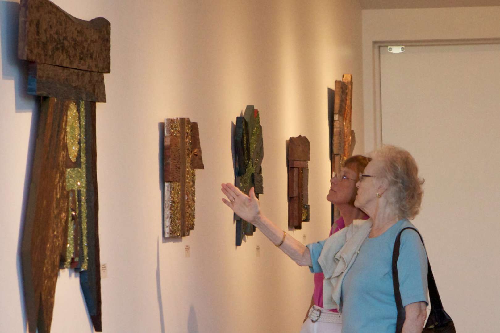Photo of Two women at the Ames Center Art Gallery Exhibition looking at sculpture on the wall