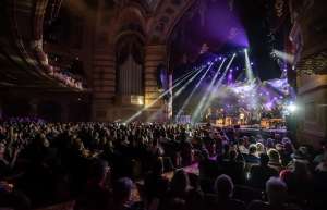 Thumbnail photo of Stage at nighttime from audience POV, large crowd and laser lights shining into crowd