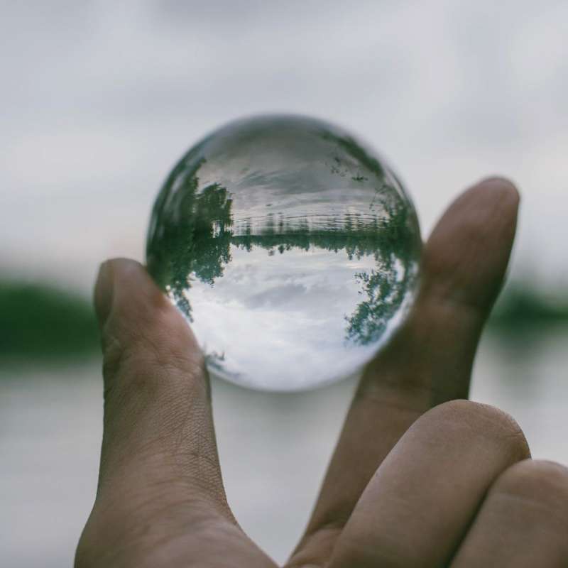 a hand holding a glass globe with reflection of the lake and sky