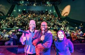 Thumbnail photo of Members of Dante's Comedy Review on Stage with the audience in the background waving and cheering