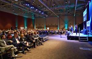 Thumbnail photo of Audience sitting at a conference in One National Events Plaza as a woman addresses them on stage