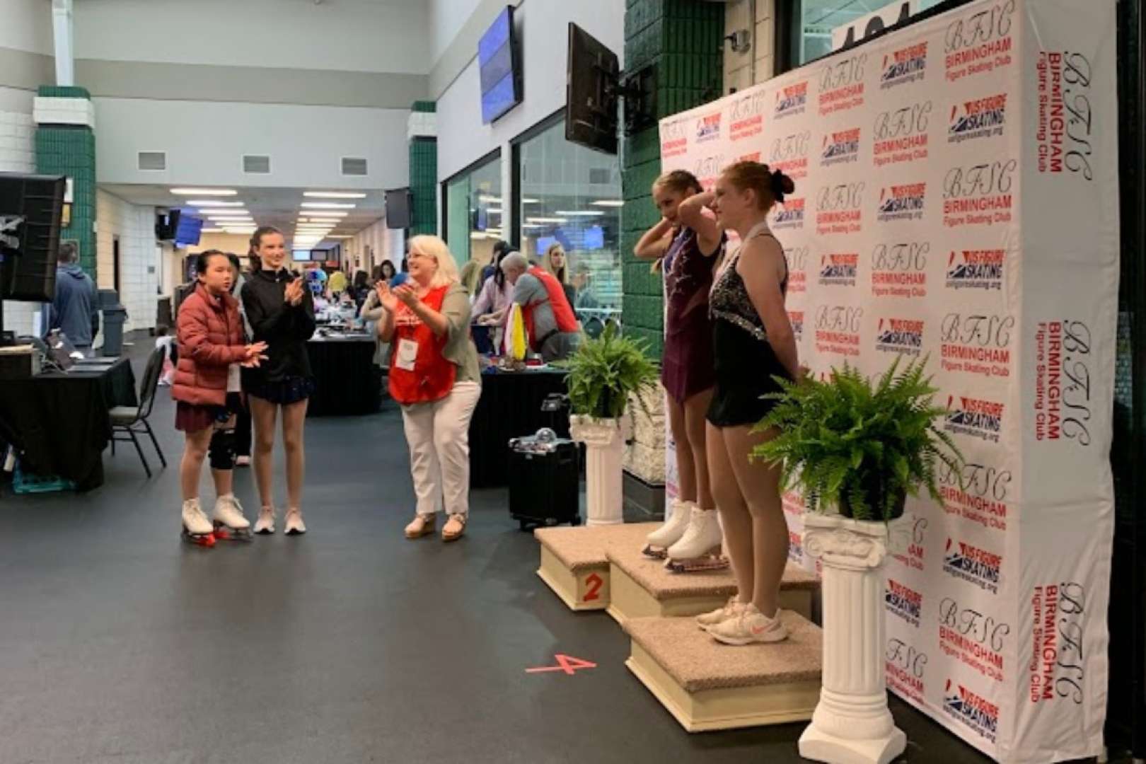 Photo of Ice skaters standing on a medal podium in front of a step and repeat