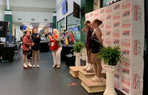 Thumbnail photo of Ice skaters standing on a medal podium in front of a step and repeat