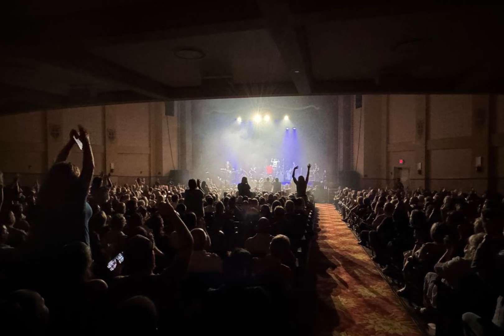Photo of Live Rock Band playing at the Sunrise Theatre with audience in silhouette and on their feet