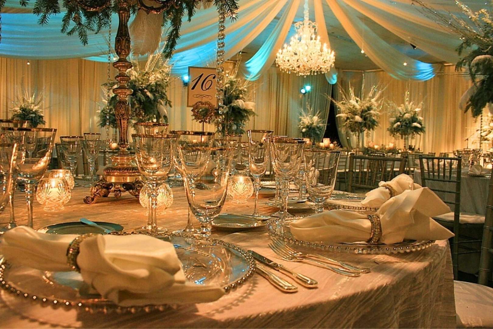 Photo of A close-up captures a beautifully arranged wedding table, elegantly set for dinner. In the background, a grand chandelier and towering floral arrangements add a touch of sophistication and charm.